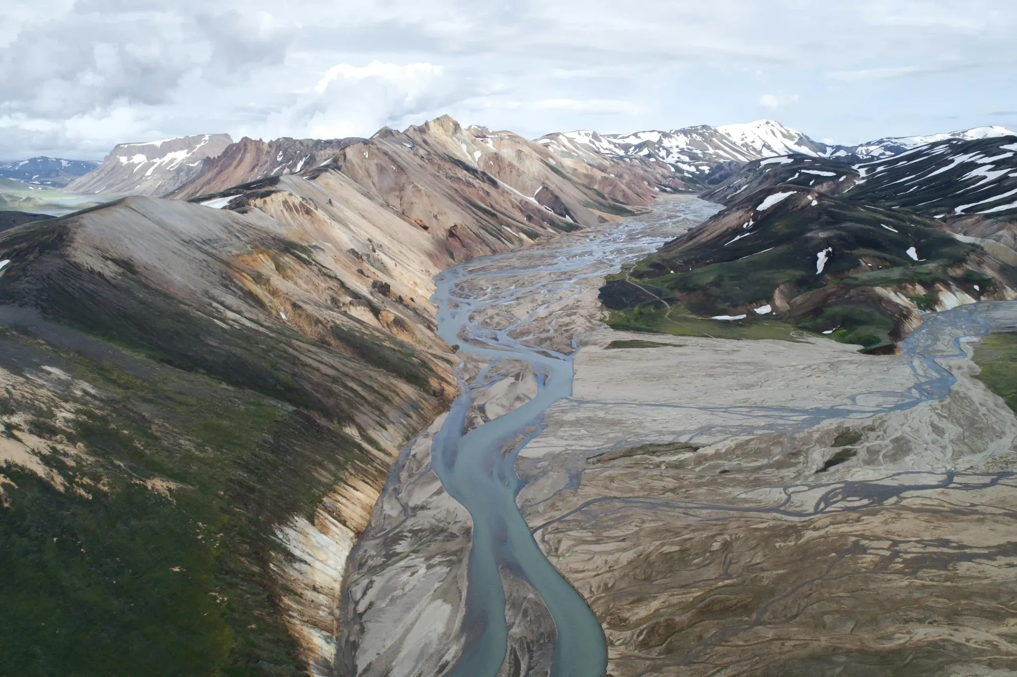 Rivière d’eau de fonte glaciaire tressant son cours à travers une plaine de cendres volcaniques dans les hautes terres de Landmannalaugar, entourée de sommets de rhyolite formés par d’anciennes éruptions islandaises